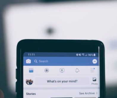 Close-up of a smartphone screen displaying a social media app. The blue header includes a search bar and icons for navigation. Below, there's a status update prompt saying "What's on your mind?" with options for stories and photos. The time is 11:11, and the phone has full signal and battery.