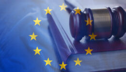 A judge’s gavel rests on a thick law book. The image is overlaid with the European Union flag, featuring a circle of twelve yellow stars on a blue background, symbolizing European law or justice.